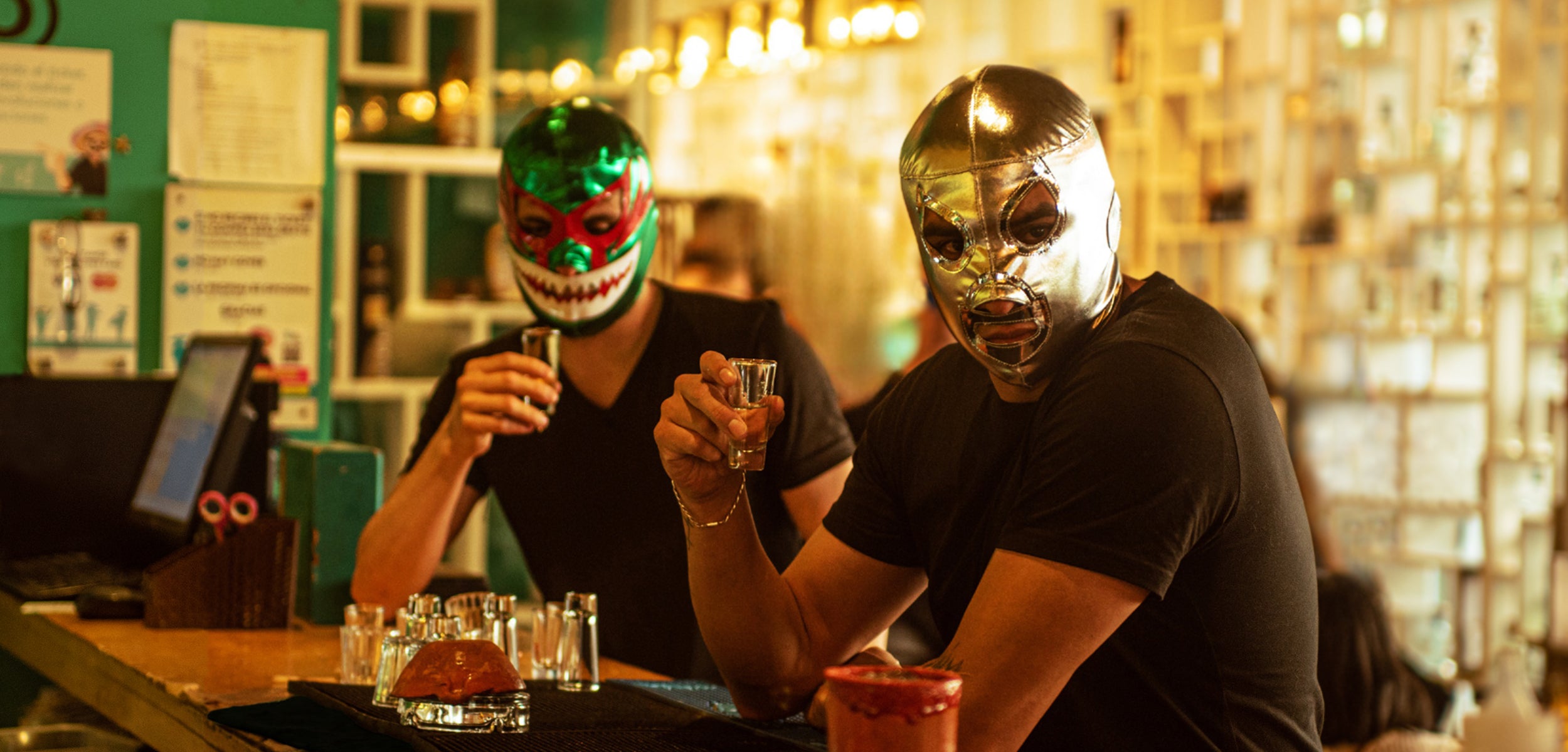 Two Men Sitting in Cantina Drinking Tequila While Wearing Lucha Libre Wrestling Masks